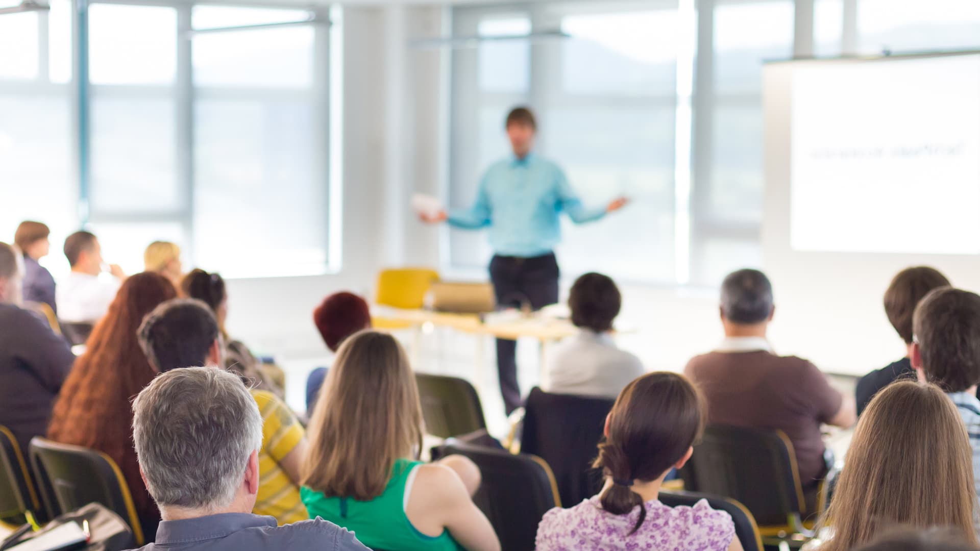 Um professor dando aula para vários alunos sentados nas suas cadeiras